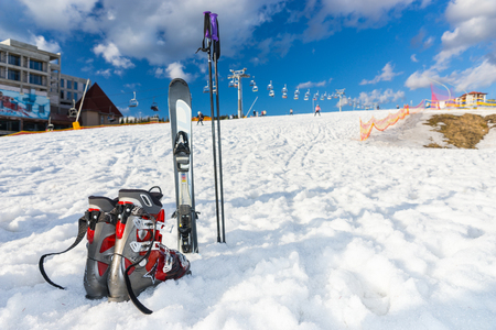 Red and gray boots next to ski laying in fluffy snow in a ski-resort in winter periodの写真素材
