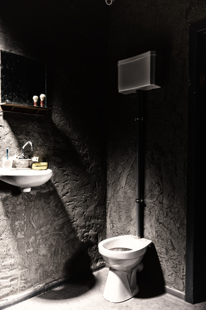 Toilet near washbasin with a soap box and toothbrush on it under the mirror with shave brush on the...
