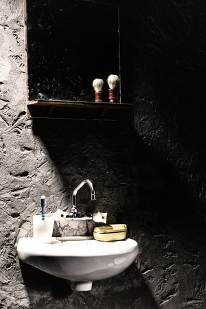 Washbasin with a mug for a toothbrush and a soap box on it under the mirror with shave brush on the shelf in a prison cellの写真素材