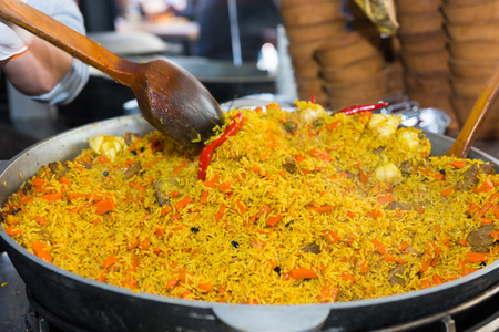 Close up of stir fry rice dish with meat and vegetables in large pot at booth at outdoor urban food festivalの写真素材