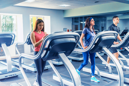 Beautiful group of young friends exercising on a treadmill at the bright modern gymの写真素材