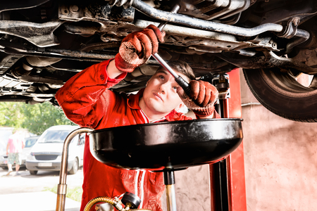 Male mechanic hooking up equipment to the undercarriage of a car elevated on a hoist during repairs and maintenance in a garage workshopの写真素材