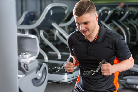 Handsome fit man training on modern row machine in gym room in fitness center