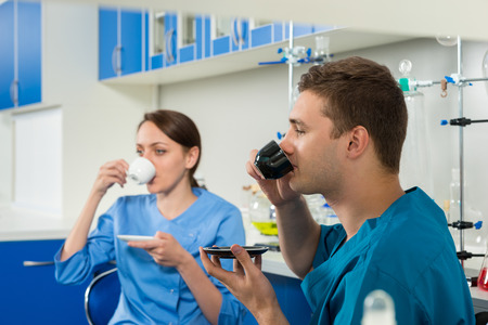 Two young scientists in uniform drinking a coffee after some research. Healthcare and biotechnology...