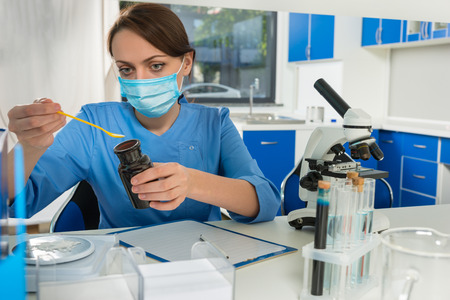 Young female scientist in uniform wearing a mask weighs powder on special scales for some research...