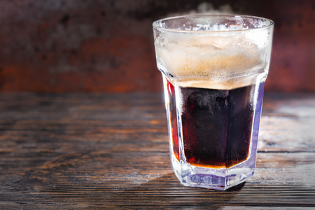 Big frozen glass with freshly poured dark beer and head of foam on wooden desk. Food and beverages conceptの写真素材