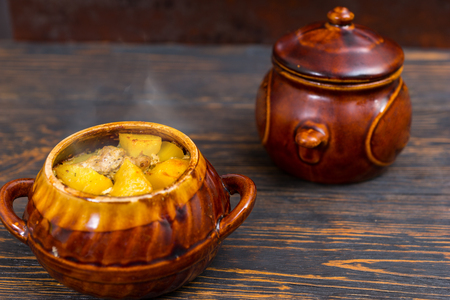 Hot roast potatoes with cheese and spices in a clay pot on a wooden desk. Food and beverages conceptの写真素材