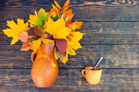 Top view of beautiful clay jug with autumn leaves and wheat near clay cup with spoon in it on aged wooden desk. Thanksgiving day and autumn conceptの写真素材