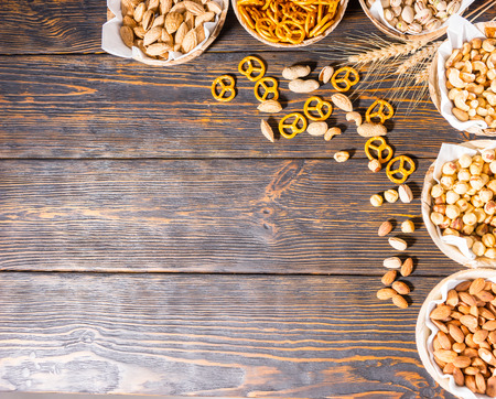 Top view of various beer snacks in plates like pistachios, small pretzels and different peanuts on dark wooden desk. Food and beverages conceptの写真素材