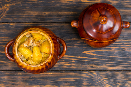 Top view of clay pots with hot roast potatoes with cheese and spices on a wooden desk. Food and beverages conceptの写真素材