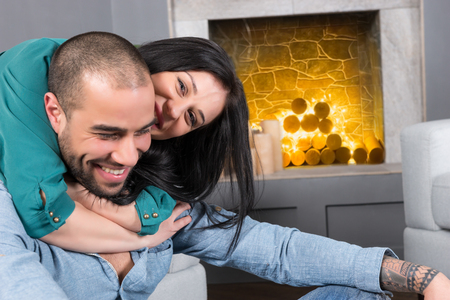 Happy international couple of man with beard and his brunette pregnant wife sitting on the sofa and...