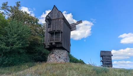 Two old historic wooden windmills on a hill top viewed from below against a sunny blue sky with white cloudsの写真素材