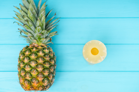 Fresh whole pineapple with leaves and canned ring or slice to the side over a blue wood background with copy spaceの写真素材