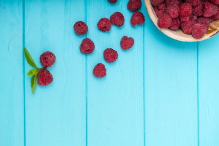 Plate of ripe raspberries with spilled fruit over a blue wooden background with copy space viewed...