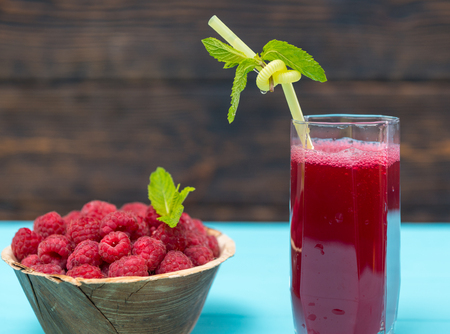 Bowl of fresh picked raspberries and glass of fruit juice with straw