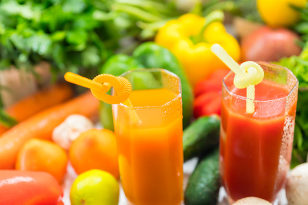 Two healthy fruit and vegetable smoothies in tall glasses surrounded by assorted fresh produce ingredients in a high angle close up viewの写真素材