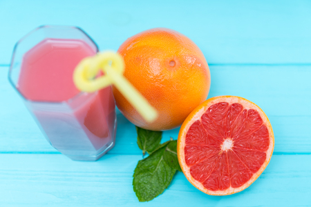 Glass of fresh grapefruit juice with whole and halved grapefruit ingredients alongside on blue wood viewed from above with focus to the fruit in a healthy diet conceptの写真素材