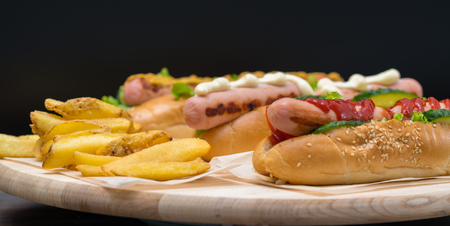 Assorted speciality hot dogs with different side trimmings and dressings served with fried potato chips on a wooden board in banner formatの写真素材
