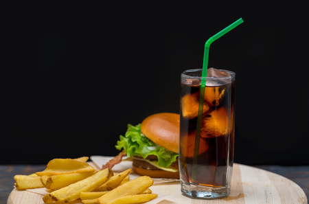 Hamburger served with French fries and a tall glass of chilled soda or coke with a straw over a dark background with copy spaceの写真素材