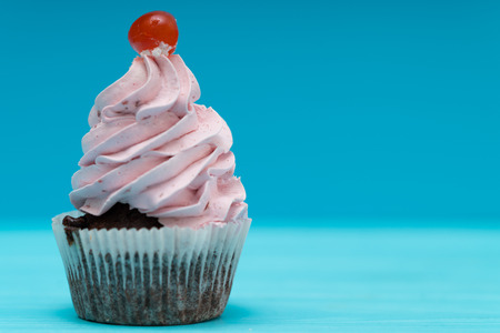 Single cupcake with twirled pink icing and cherry on a blue background with copy spaceの写真素材