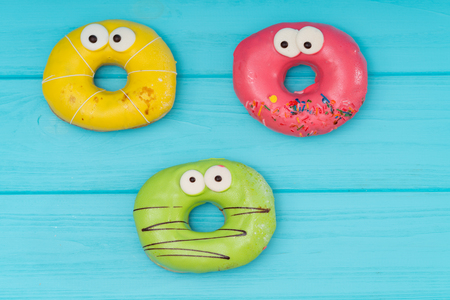 Three colorful iced donuts with eyes arranged on a blue wooden background with copy spaceの写真素材