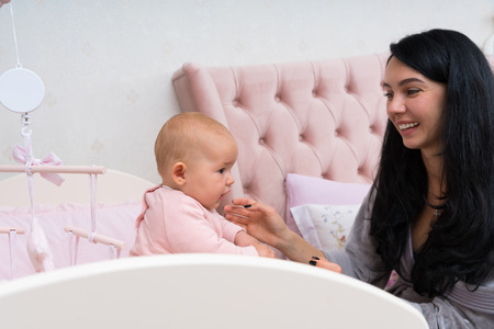 A happy, loving mother playing with her baby in pink crib setting with hanging mobile.
