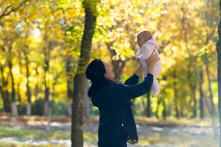A happy mother holding her baby playfully in the air in bright autumn park scene.の写真素材