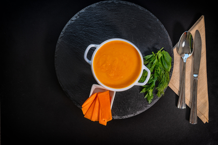 Delicious creamy thick healthy pumpkin soup with herbs served in a white bowl on a black background for a vegetarian starter to a mealの写真素材