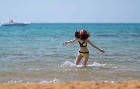 Joyful young woman splashing in the sea tossing her long hair in the breeze on a sunny tropical beach on summer vacationの写真素材