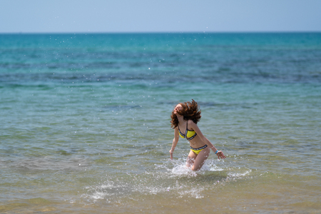 Carefree young woman in a bikini frolicking in the sea tossing her long hair as she splashed through the shallowsの写真素材