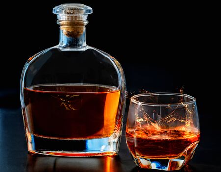 Close up on a glass of whiskey with splash effect in front of a corked decanter over a dark background with copy spaceの写真素材