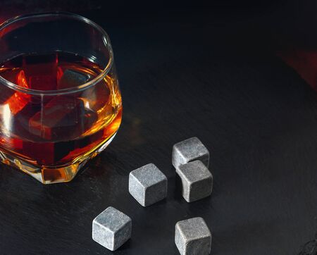 Close-up of cubical grey stones for alcoholic beverages on the counter next to a glass of cognac viewed from high angle on dark backgroundの写真素材