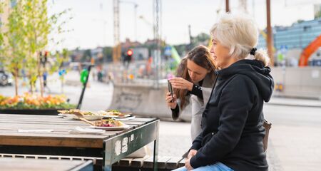 Young woman photographing food on a mobile phone as the family eat at an outdoor restaurant on a city streetの写真素材
