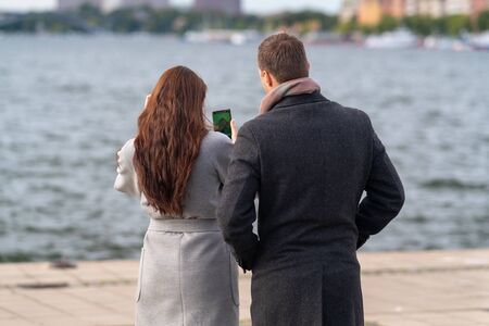 Young couple checking a photograph on their mobile phone as they stand in warm winter overcoats on a...