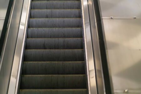 Close up on the treads of an empty moving escalator in a subway or mall with reflection on the steel...