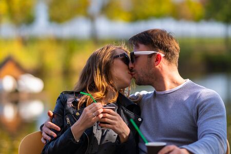Romantic young couple sitting arm in arm at a table at a restaurant kissing outdoors as they enjoy a coffee togetherの写真素材