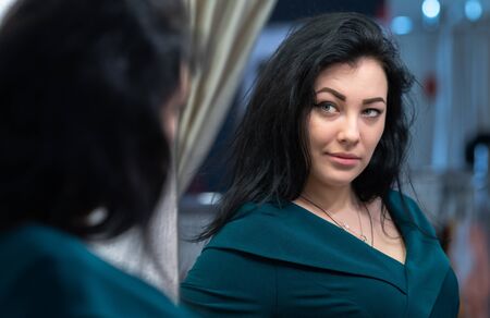 Attractive dark haired woman looking at her reflection in a mirror in an over the shoulder view with...