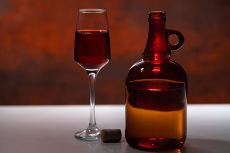 Decanter and stylish glass of red wine on a counter with cork against a glowing reddish brown background in a close up side viewの写真素材