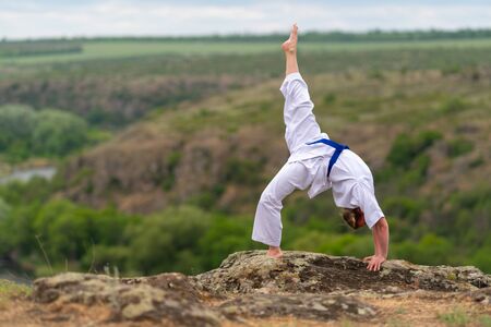Athletic young martial arts woman working out doing a backward stretch on a rock overlooking a valley below in a health and fitness conceptの写真素材