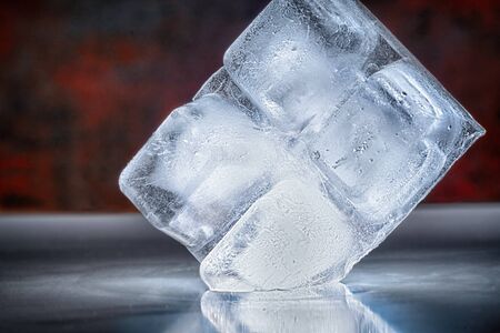 Four ice cubes in a block placed on edge balancing on the corner on a reflective bar counter in a...