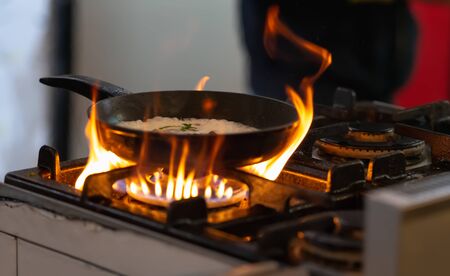Pan of food sizzling on a gas hob over hot flames in a kitchen in a catering conceptの写真素材