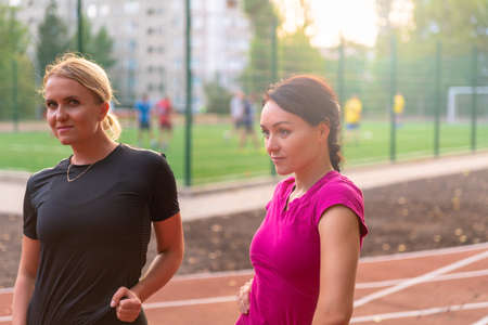 Two attractive young woman on a sports track at an open air sports arena looming to the side with thoughtful expressions in a health and fitness or active lifestyle conceptの写真素材