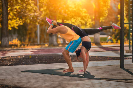 Young couple doing acrobatic gymnastics outdoors backlit by the warmth of the morning sun doing a handstand splits in a health and fitness conceptの写真素材