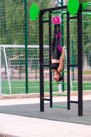 Young woman hanging from a gym ladder at an outdoor sporting facility in summer in a health and...