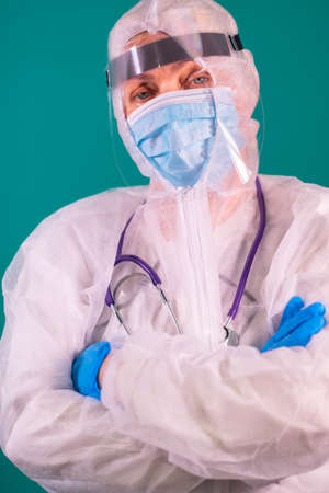 Physician with a face shield in PPE suit uniform with stethoscope on the shoulder, standing with arms crossedの写真素材