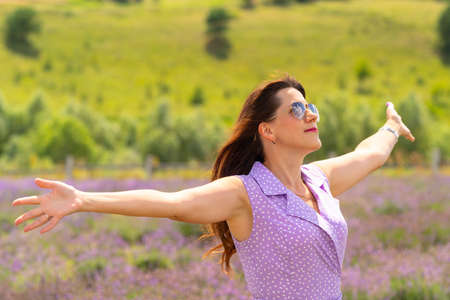 Happy woman rejoicing in the warm summer weather holding out her arms as she faces the sun with a smileの写真素材