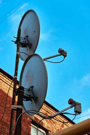 Two satellite dishes installed at home looking at blue skyの写真素材