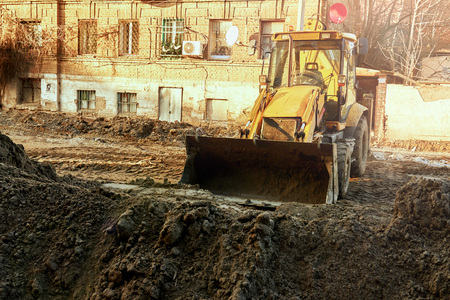 A large yellow excavator in the city digs a pit with a bucketの写真素材
