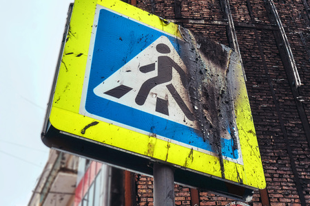 A square sign of a pedestrian crossing on a street in a big city after a violent fire from a nearby house was burnt, blackened and sported after thatの写真素材