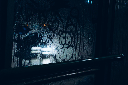 A sad drawing on the sweaty glass of a child's bear with hearts against the light of headlights